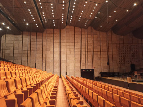 A concert hall – view into the auditorium with a tiered seating; the side panelled wall integrates a glassed parts to the recording studio