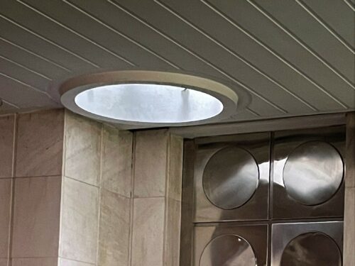 The circular skylights in the ceiling and the steel door leading to the rear part of the bar correspond with the overall shaping of the interior