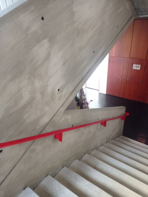The solid mass of the concrete staircase is accentuated by a colourful steel handrail 