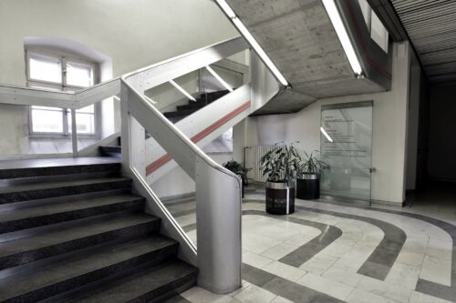 The concrete flights of the staircase are complemented by atypically sculptured railings, accentuating the red lines and timeless linear luminaires