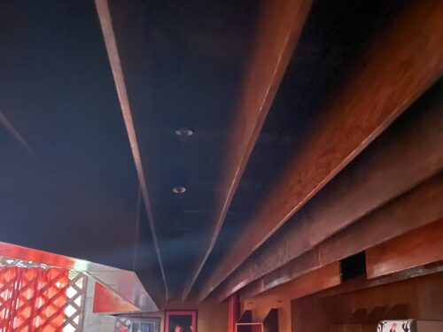 The massive ceiling slats delineate visually the bar area; on the background, there is a visible part of additionally mounted divider made of diagonally laid wooden profiles