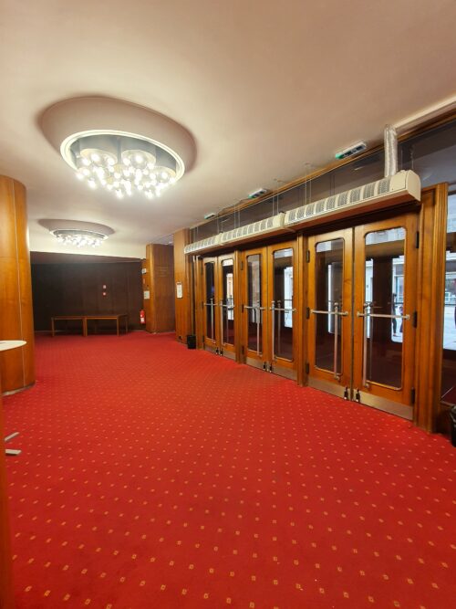 The interior of the entrance foyer is complemented by wooden wall and column panelling, a shaped gypsum ceiling with lights and a carpet of a distinctive red colour