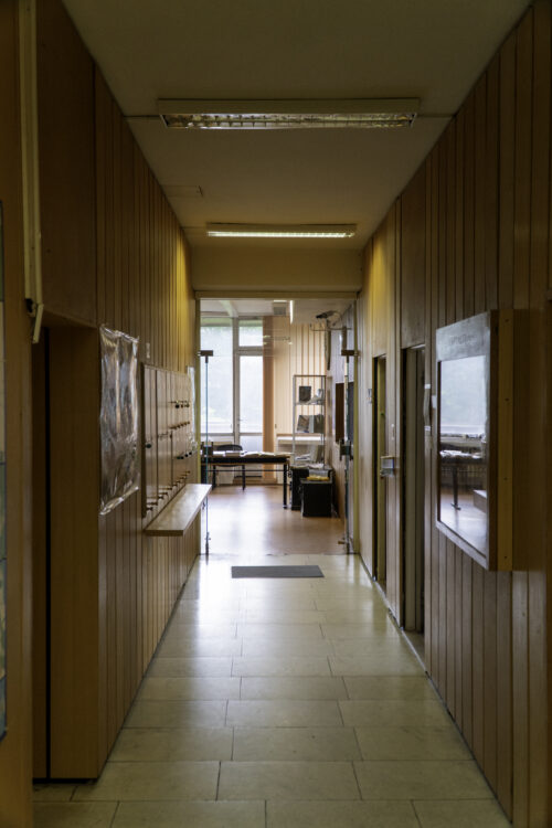 The materiality of wood and white wall and floor surfaces is also present in the corridor leading to the research room