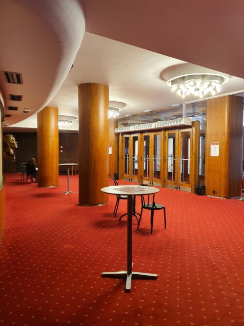 Interiér vstupného foyera dotvárajú drevené obklady stien a stĺpov, tvarovaný sadrový strop so svietidlami a koberec výraznej červenej farby