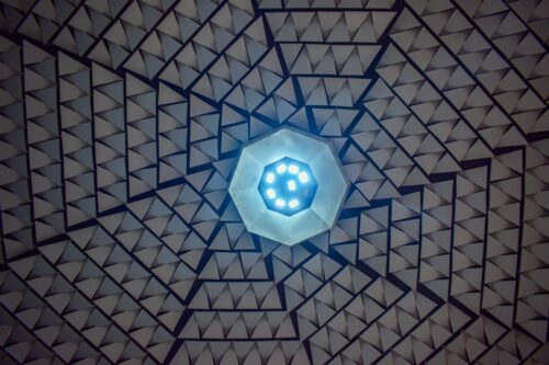 Výrazovou dominantou auly je strešná rovina, ktorú dotvára geometrická hra trojuholníkových podhľadových platní a centrálne situovaný svetelný objekt