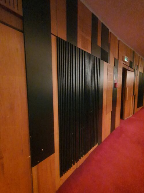 The rounded walls of the theatre hall are decorated with wooden panels in natural and black-stained finishing 