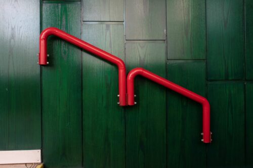 The colour-accentuated steel tubes of the handrail dominate the wooden panelling's green surface