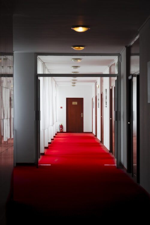 The interior of the corridor leading to hotel rooms is dominated by the building interior’s tectonics and a carpet in accentuating red colour